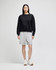 A black crewneck sweatshirt worn with grey shorts, paired with white sneakers, featuring branding.