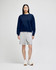 A navy crewneck sweatshirt worn with grey shorts and white sneakers, featuring a logo on the sweatshirt.