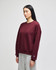 A maroon women's crewneck sweatshirt with a relaxed fit, featuring a logo on the sleeve. Styled with grey pants.