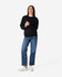 A black crewneck sweatshirt is worn by a person paired with blue jeans and white sneakers, featuring a logo.