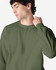 An olive green Gildan Heavy Blend adult crewneck sweatshirt with a model showcasing its fit and design.