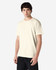 A man models a beige Gildan Heavy Cotton Adult T-Shirt, with a minimalistic design and short sleeves.