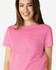 A pink Gildan Heavy Cotton Ladies' T-Shirt displayed on a smiling woman, featuring a simple design and a logo.