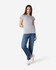 A grey ladies' t-shirt is worn with blue jeans and white sneakers, showcasing a casual outfit. The t-shirt has a logo.