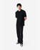 A model wearing a black Gildan Softstyle Adult Double Pique Polo, paired with dark jeans and sneakers.