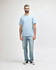 A midweight adult T-shirt in light blue, worn by a model with dark pants and sneakers, featuring a logo.