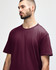 A man wearing a burgundy Gildan Softstyle adult midweight t-shirt, featuring a simple design and short sleeves.