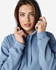A hooded sweatshirt in a soft blue shade, featuring a drawstring and a relaxed fit, worn by a model.