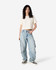 A woman stands in a beige boxy t-shirt and light blue cargo jeans, featuring a logo on the shirt.