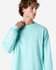A turquoise heavyweight cotton unisex long sleeve T-shirt on a model, featuring a logo on the sleeve.