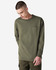 A long-sleeve, olive green t-shirt featuring a pocket and a logo, modelled by a young man.