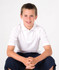 A white kid's pique polo shirt featured on a young boy, seated and smiling, wearing dark shorts. The shirt has a logo.