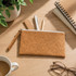 A cork pencil case with a zippered closure, surrounded by pens, a ruler, a notepad, and a cup of coffee.