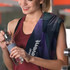 A full-colour gym towel in dark tones draped over a woman's shoulder, with a drink bottle in her hand.