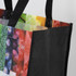 A black tote bag with a colourful, patterned interior featuring various fruits and vegetables. It has sturdy handles.