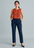 A woman in an orange sleeveless top and navy tapered leg adjustable waist pants, standing with hands in pockets.