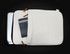 A cream-coloured laptop sleeve with leather accents, showing a partially open compartment and a notebook inside.
