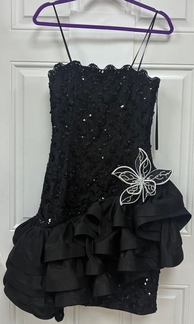 A classic black sequin mini dress from the 80s, finished with a delicate white flower detail for a soft, romantic contrast. A rare vintage collector's piece that brings retro party glamour to any night out or special occasion.