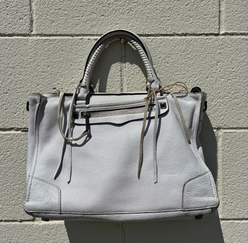 Soft, buttery leather meets a structured silhouette with polished gold-tone hardware and a clean, crisp white finish. Featuring dual rolled handles plus a detachable, adjustable crossbody strap, this satchel transitions effortlessly from work to weekend. Roomy interior with slip and zip pockets keeps essentials organized on the go.
