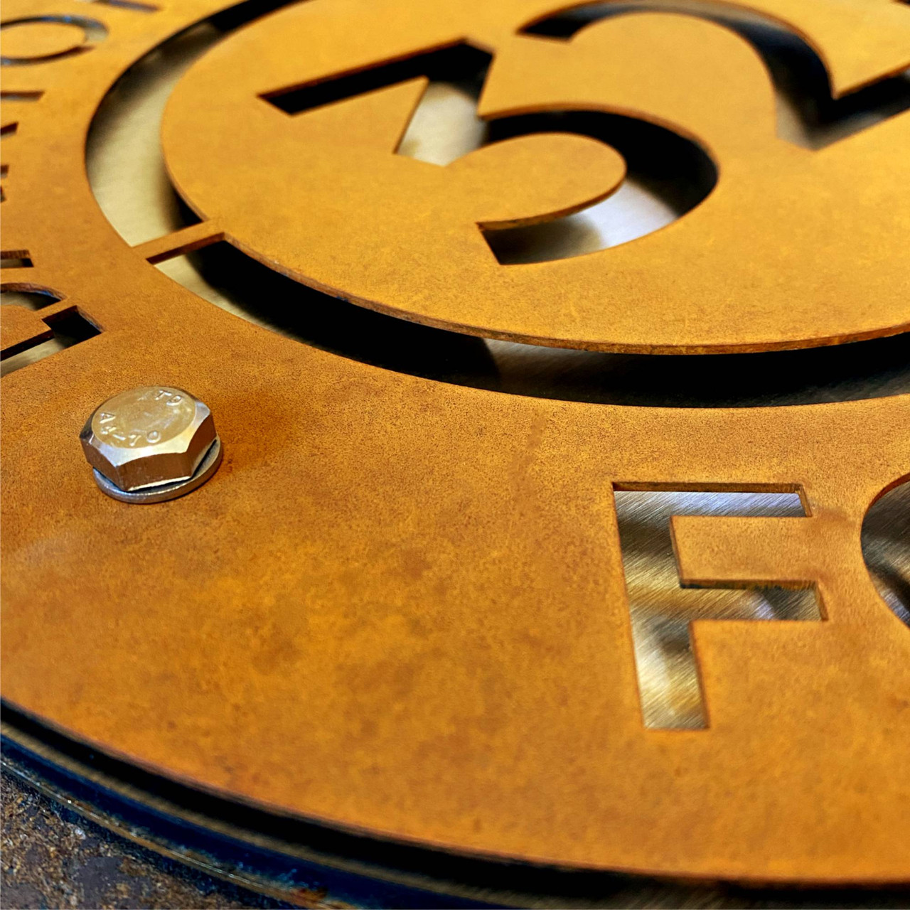 Circular Corten steel projecting sign with stainless steel middle layer