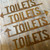 Rusty steel toilet sign with directional arrow.