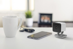 Wi-Fi security camera on a desk beside a smartphone showing app connectivity