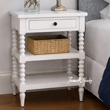 An angled detailed view of the Montclair Side Table in White showcasing its bobbin leg detailing and functional drawer and display shelving.