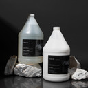 Amenie Sicilian Tangerine Shampoo, Conditioner, and Lotion gallon bottles on a black stone spa surface
