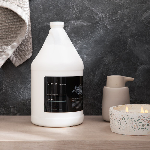 Amenie Sicilian Tangerine Lotion gallon bottle displayed with towel and soap dish for luxury bathroom setting