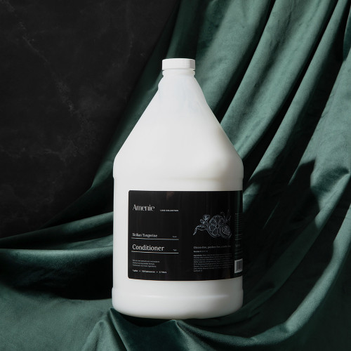 Amenie Sicilian Tangerine Conditioner gallon bottle styled on emerald green satin fabric for a luxurious spa aesthetic