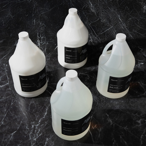 Amenie Sicilian Tangerine personal care gallon collection with black labels, styled on a stone surface for a spa-inspired aesthetic
