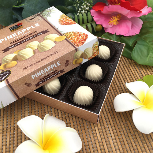 Ed & Don's Pineapple White Chocolate Covered Macadamia Nuts. Showcasing the open box with a white and yellow plumeria display