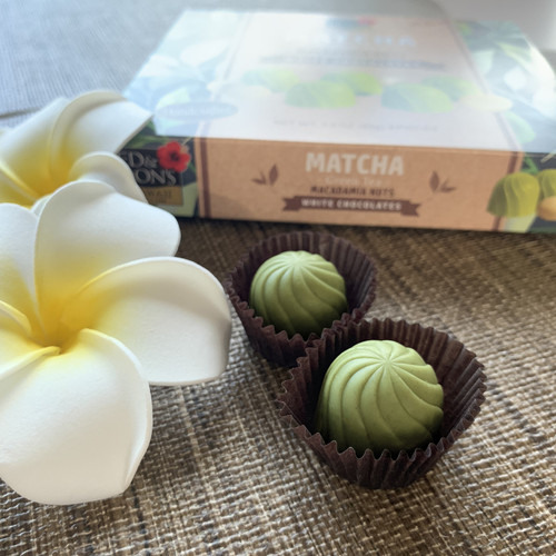 Ed & Don's Match Green Tea White Chocolate Covered Macadamia Nuts. Showcasing the actual chocolates with a white and yellow plumeria display