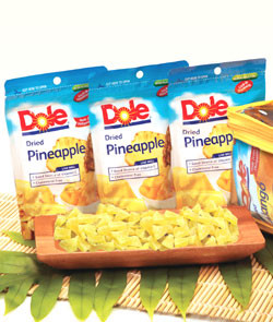 Dole Plantation Dried Pineapple Pouches showcased behind a monkeypod serving plate of dried pineapple chunks