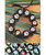 Black Kukui Nut bracelet laid on a wooden table with decorative flora underneath. The bracelet has Painted Hibiscus flowers in pink. Painted Kukui Nuts are arranged below in the following colors from left to right: yellow, purple, red, white, and blue.