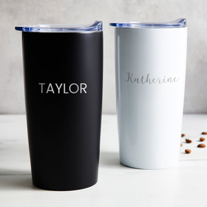 Personalized stainless steel coffee tumbler in black or white laser engraved with your name in your font choice, displayed on table.