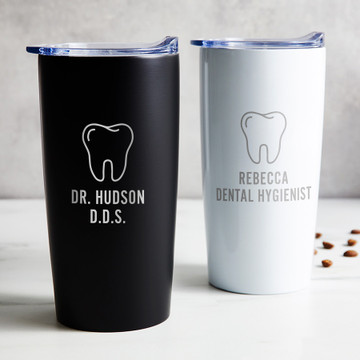 Personalized Dentist stainless steel coffee tumbler in black or white laser engraved with tooth design and your name and title, displayed on table.