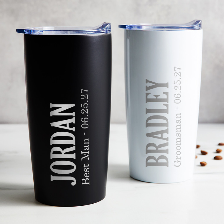 Personalized Groomsman stainless steel coffee tumbler in black or white laser engraved with their name, wedding role, and wedding date, displayed on table.