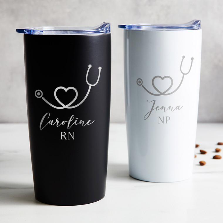 Personalized Nurse and Medical Professional stainless steel coffee tumbler in black or white laser engraved with stethoscope heart design and you name and title, displayed on table.