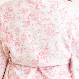 Close-up of pink toile robe fabric with floral and bow print and soft plush texture