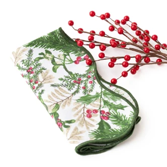 Folded cotton dinner napkin with a woodland berry and holly print and a scalloped green edge (alternate angle)