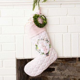 Blush pink quilted Christmas stocking with a velvet cuff, wreath, and nutcracker embroidery, hung on a mantel