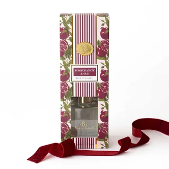 Pomegranate & Oud reed diffuser with a glass vessel, gold collar, and reeds in a striped gift box (alternate angle)