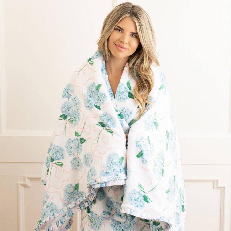 8 Oak Lane hydrangea ribbons luxe throw blanket 56 x 60 inches with blue floral print and pink ribbon detail (lifestyle view)