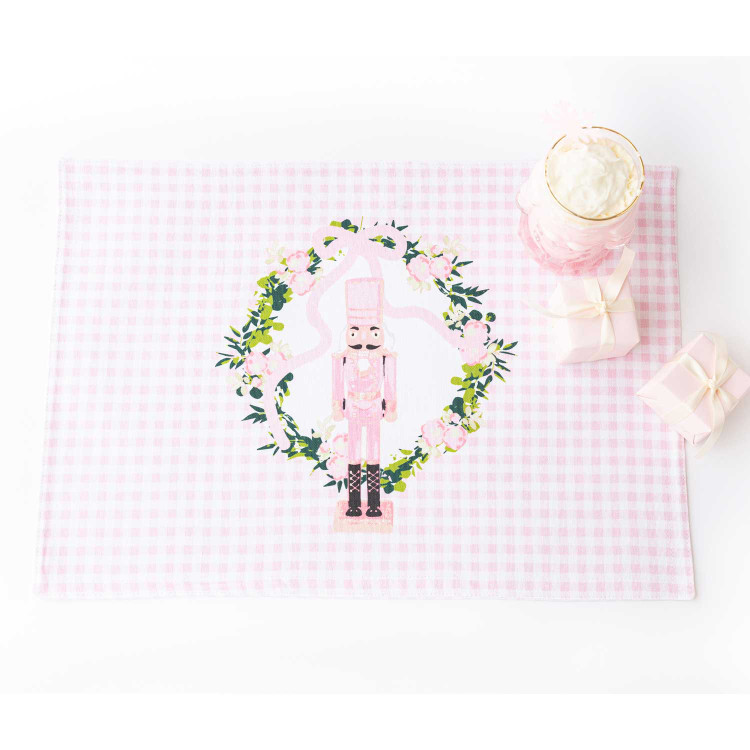 Pink gingham reversible placemat with a nutcracker in a floral wreath print, styled with holiday gifts