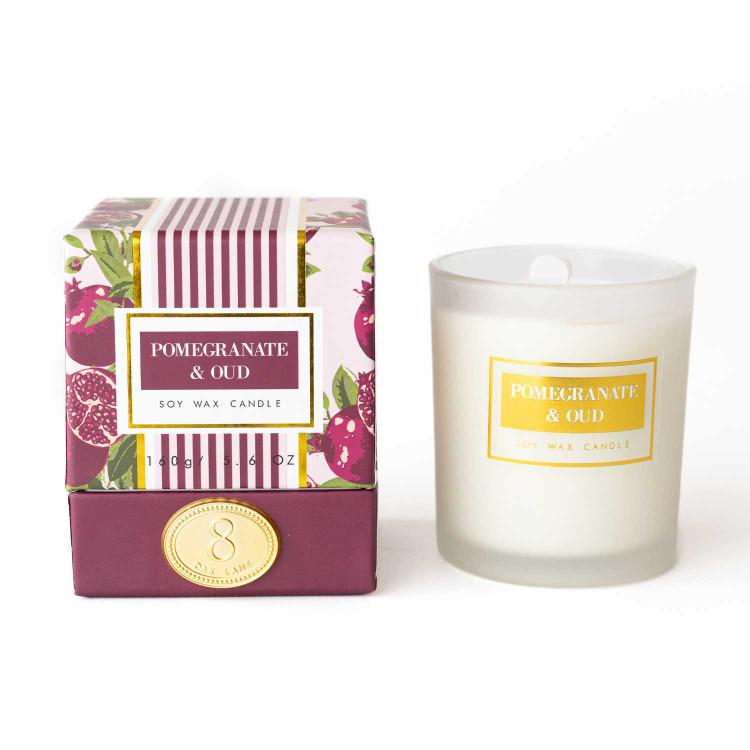 Pomegranate & Oud soy candle in a pink pomegranate-print gift box, shown next to the frosted glass candle