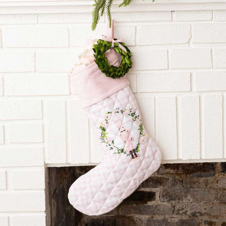 Blush pink quilted Christmas stocking with a velvet cuff, wreath, and nutcracker embroidery, hung on a mantel