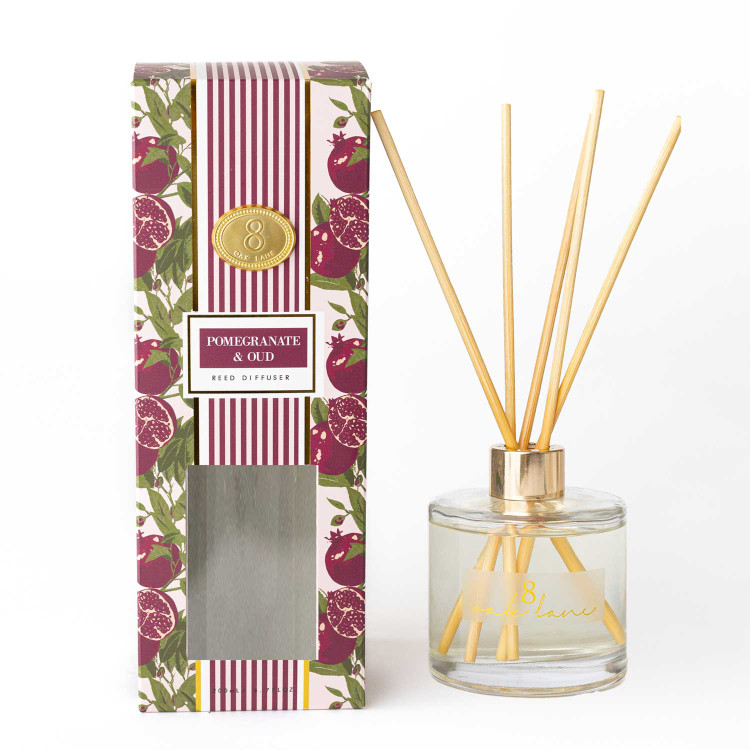 Pomegranate & Oud reed diffuser with a glass vessel, gold collar, and reeds in a striped gift box