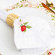 Table setting with white dinner napkin featuring botanical berry embroidery and soft neutral styling (lifestyle view)