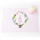 Pink gingham reversible placemat with a nutcracker in a floral wreath print, styled with holiday gifts (additional product view)